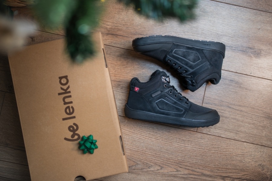 Schwarze beliebteste Barefoot Schuhe auf Holzboden neben einer Be Lenka Geschenkbox.