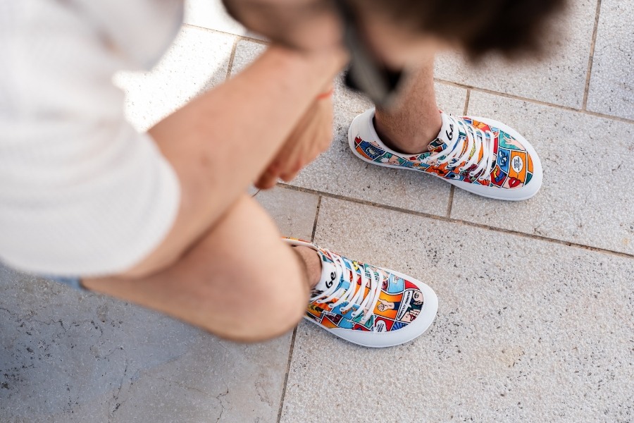 Vue de dessus de pieds en chaussures barefoot pour homme colorées à motifs sur un pavage Vue de dessus de pieds en chaussures barefoot pour homme colorées à motifs sur un pavage