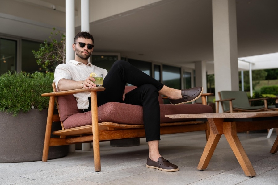 Homme en chaussures barefoot pour homme marron assis dans un fauteuil sur une terrasse Homme en chaussures barefoot pour homme marron assis dans un fauteuil sur une terrasse
