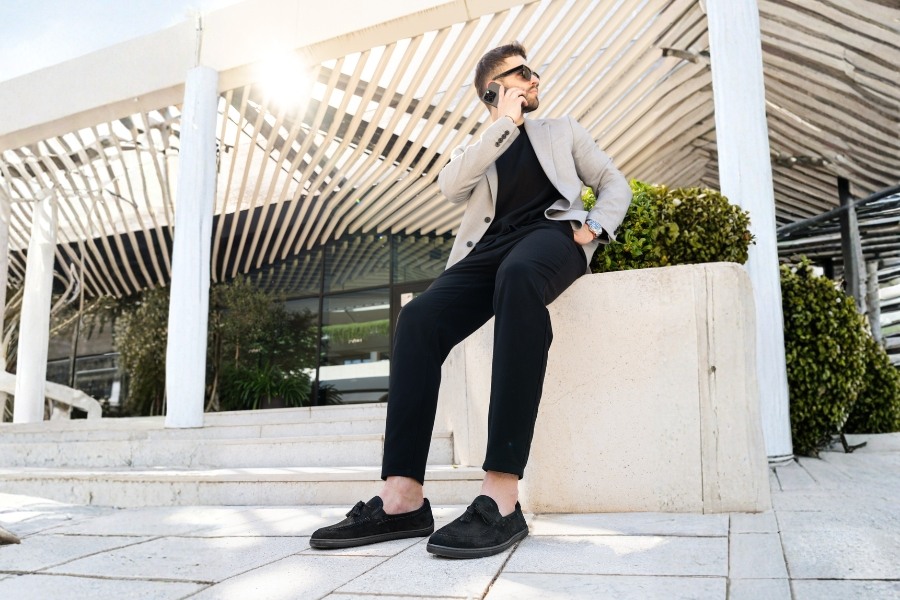 Man in black suede men's barefoot moccasins sitting on a wall in the city Man in black suede men's barefoot moccasins sitting on a wall in the city