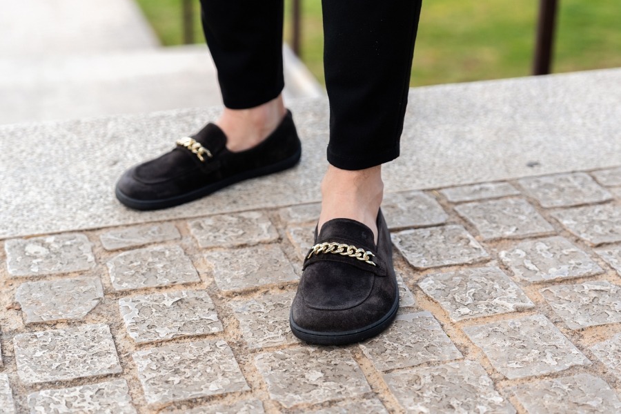 Close-up of feet in black suede men's barefoot moccasins with a chain detail Close-up of feet in black suede men's barefoot moccasins with a chain detail