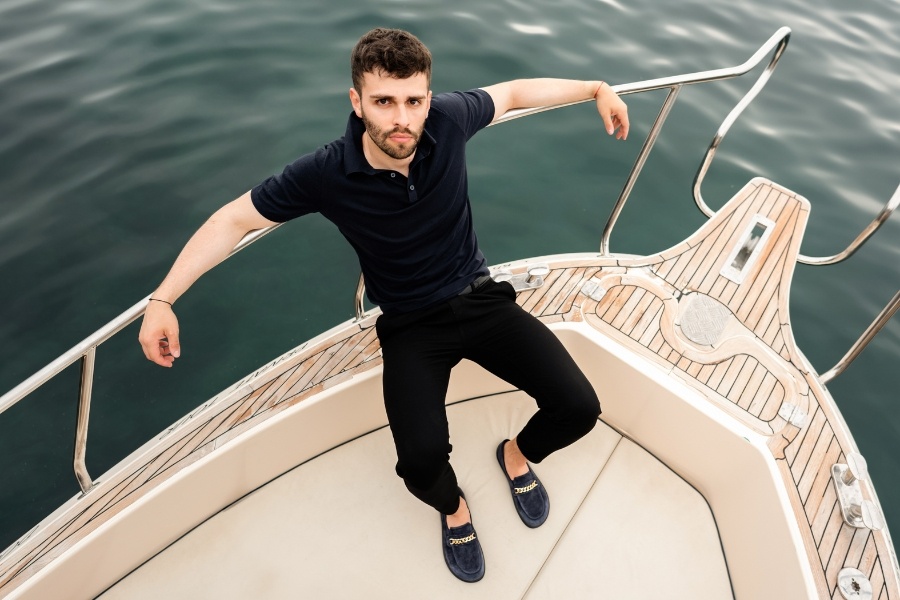 Man in navy men's barefoot moccasins standing on a boat by the water Man in navy men's barefoot moccasins standing on a boat by the water