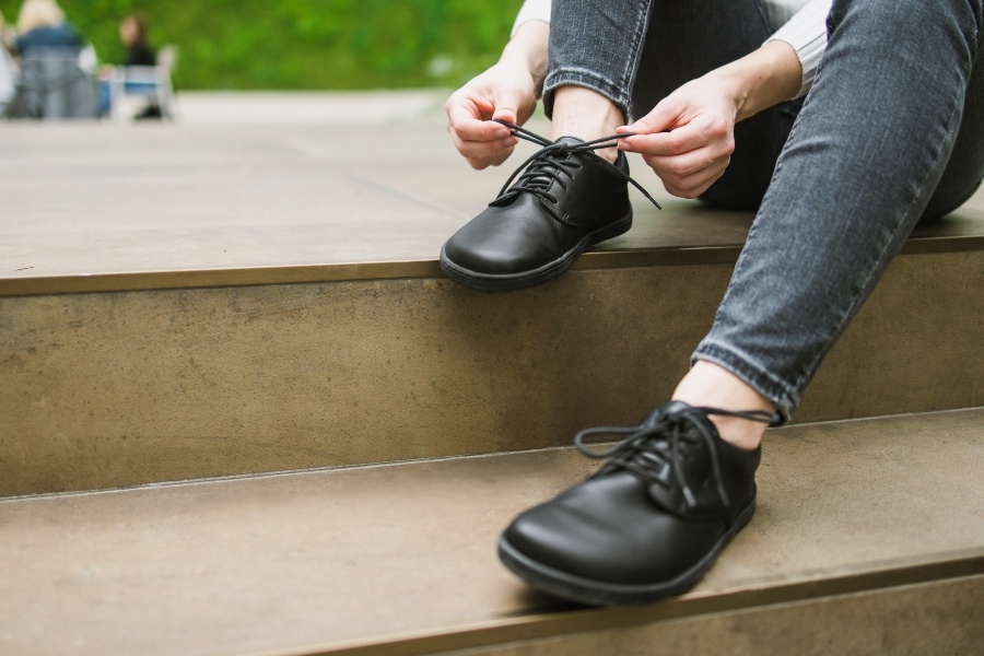 Gros plan du laçage de chaussures basses barefoot pour homme en cuir noir sur des marches Gros plan du laçage de chaussures basses barefoot pour homme en cuir noir sur des marches