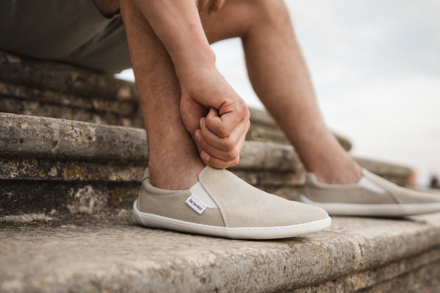 Man putting on beige men's slip-on barefoot shoes on stone steps Man putting on beige men's slip-on barefoot shoes on stone steps