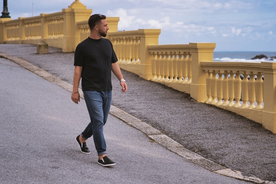 Man in black men's slip-on barefoot shoes walking along a seaside promenade Man in black men's slip-on barefoot shoes walking along a seaside promenade