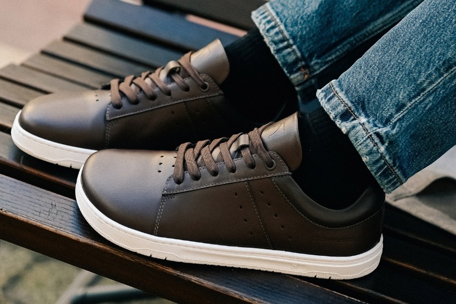 Close-up of feet in dark brown leather men's barefoot sneakers on a wooden bench Close-up of feet in dark brown leather men's barefoot sneakers on a wooden bench