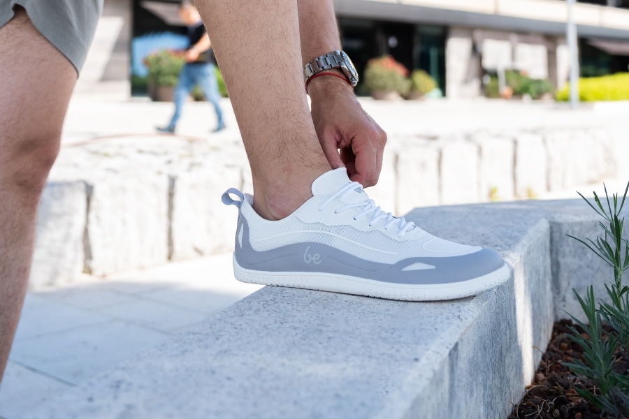 Man lacing up white and grey men's spring barefoot shoes on a stone wall Man lacing up white and grey men's spring barefoot shoes on a stone wall