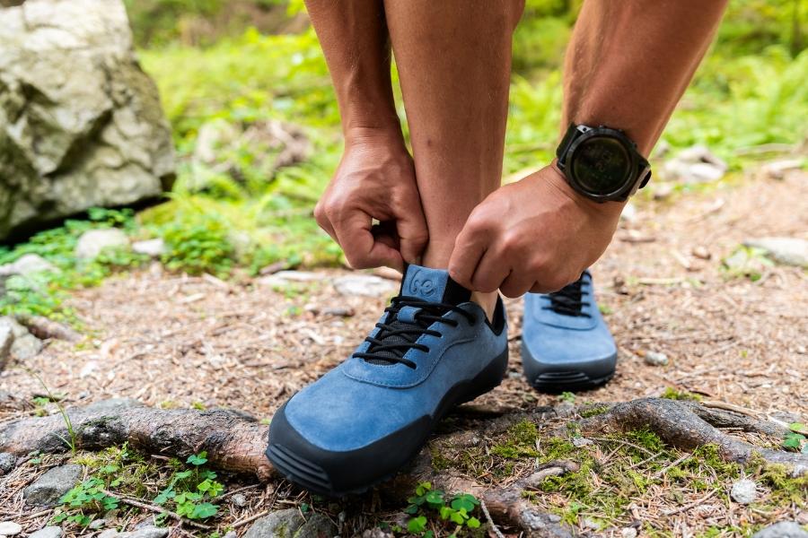 Man lacing up blue men's outdoor barefoot shoes on natural terrain Man lacing up blue men's outdoor barefoot shoes on natural terrain
