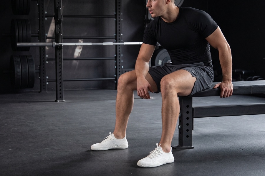 Man in white men's sports barefoot shoes sitting on a bench in a gym