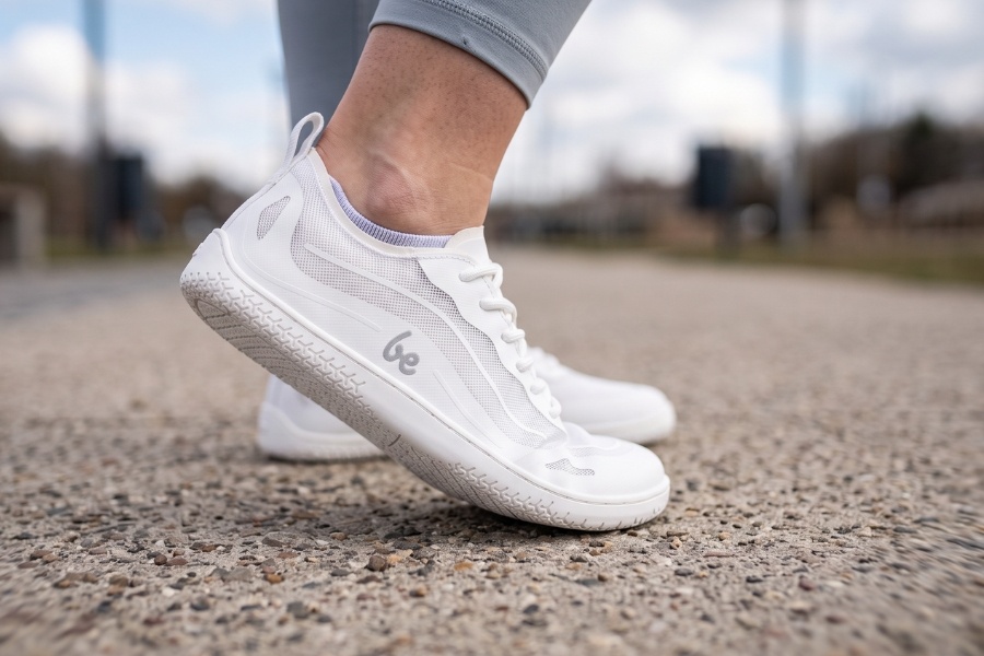 Primer plano de zapatos barefoot deportivos blancos de suela flexible y puntera ancha sobre grava. Primer plano de zapatos barefoot deportivos blancos de suela flexible y puntera ancha sobre grava.