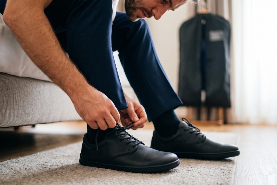 A person in a navy suit lacing up black barefoot wedding shoes before the ceremony. A person in a navy suit lacing up black barefoot wedding shoes before the ceremony.